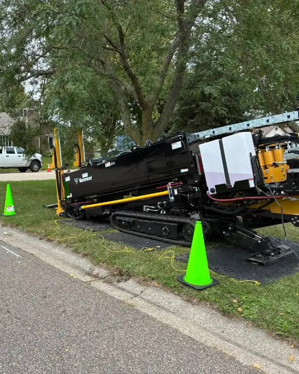A black Vermeer directional drill set up on a corner lawn, with traffic cones and mats under the tracks.